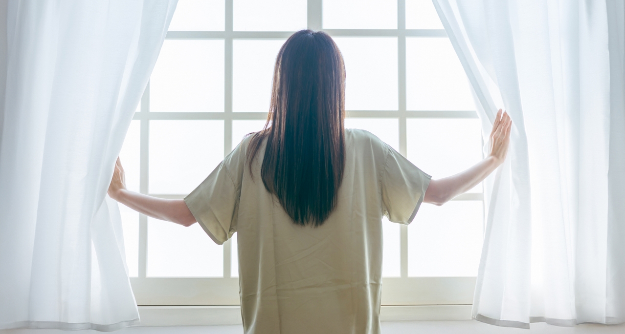 窓辺でカーテンを開ける女性の後ろ姿